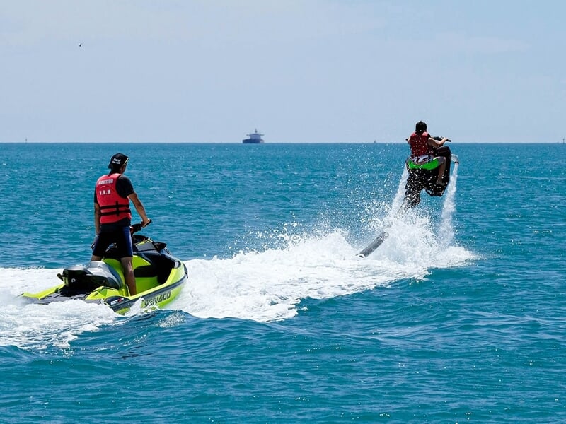 Un homme en jetski et un autre en flyride sur l'eau avec un bateau en fond