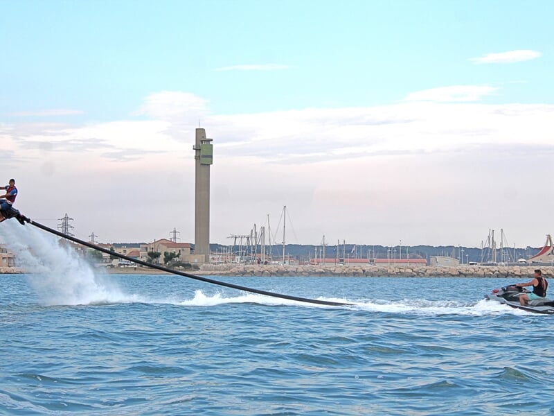 Un homme pratiquant le flyride avec la côte en arrière plan et le jetski qui l'accompagne