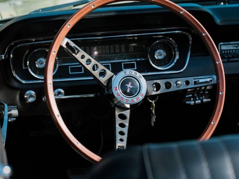 Un gros plan sur un volant vintage, probablement en bois ou en métal chromé, avec un tableau de bord au style rétro et des compteurs classiques.