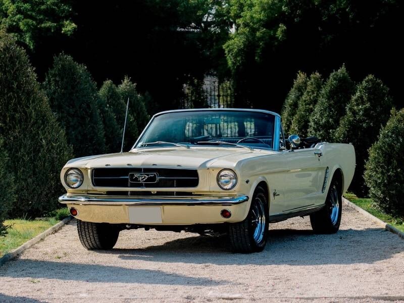 Une voiture décapotable ancienne, prise en photo dans un cadre ensoleillé. Elle arbore sans doute une carrosserie brillante et un design intemporel.