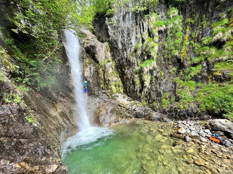 Personne effectuant une descente en rappel tout près d'une cascade