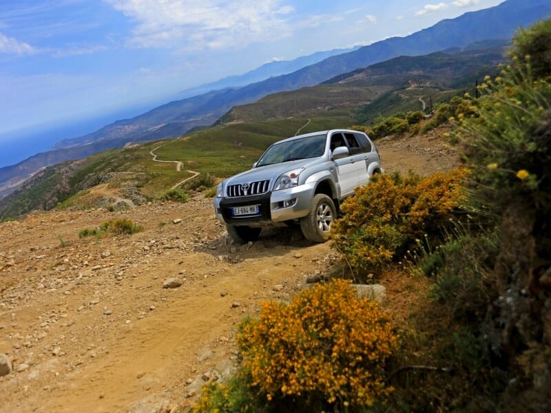 4x4 gris dans une pente en terre, entourée de buissons et avec une vue sur les montagnes