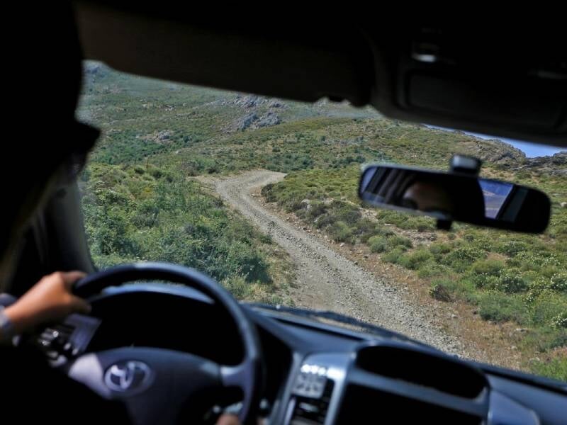 Vue sur la nature et une piste de terre à travers le parbrise avant d'une voiture avec un homme au volant