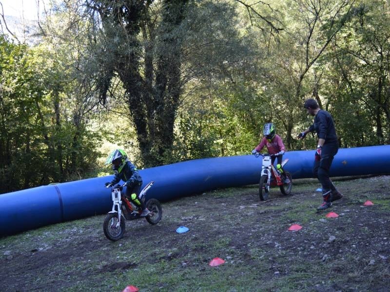 Deux enfants chacun sur une moto trial électrique, en train de rouler sous les conseils du moniteur qui les supervise