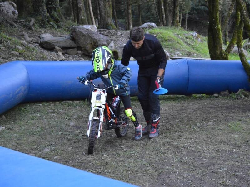 Un enfant sur une moto trial électrique accompagné par un moniteur qui tient la moto par l'arrière