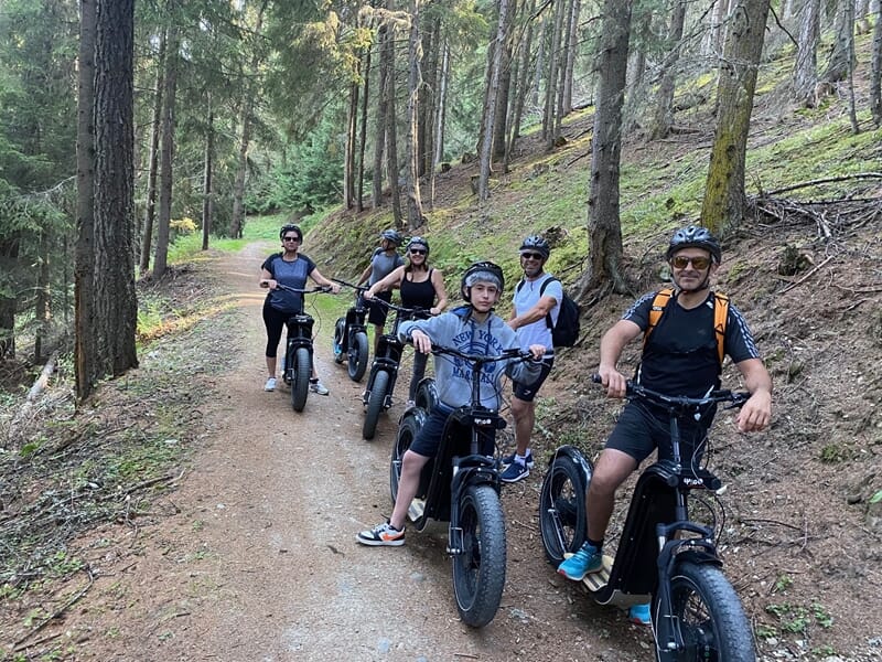 Groupe de personnes pratiquant la trottinette électrique en montagne sur chemin en forêt