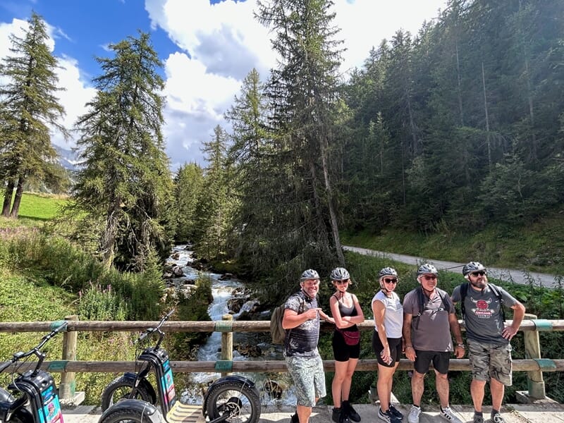 Groupe de personnes pratiquant la trottinette électrique en montagne prenant la pause sur un pont