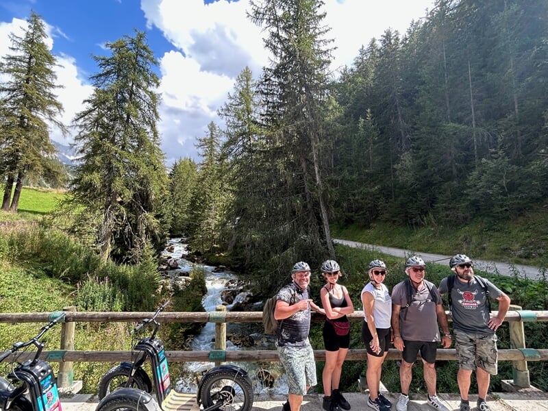 Groupe de personnes pratiquant la trottinette électrique en montagne prenant la pause sur un pont