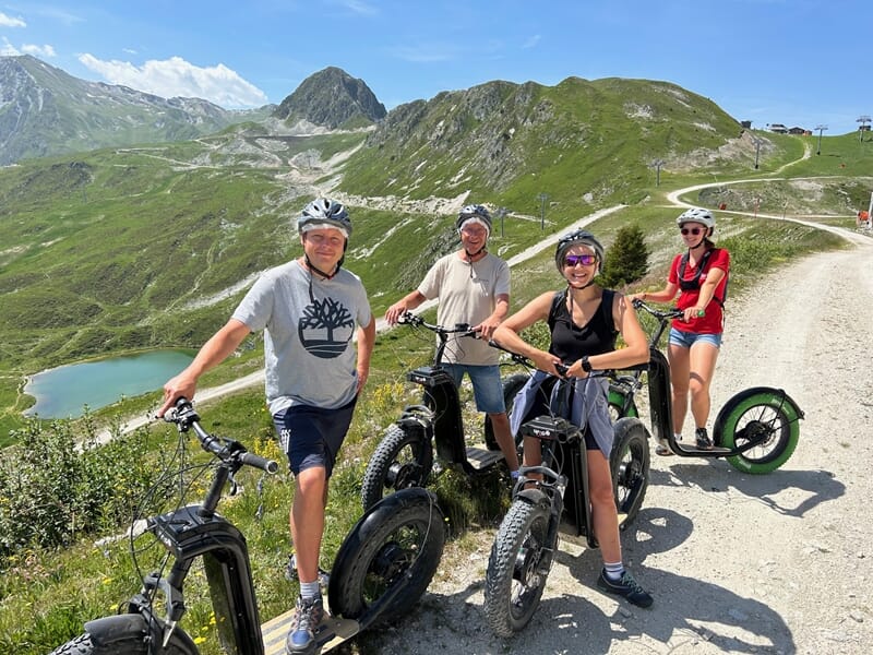 Groupe de personnes pratiquant la trottinette électrique en montagne avec lac en fond