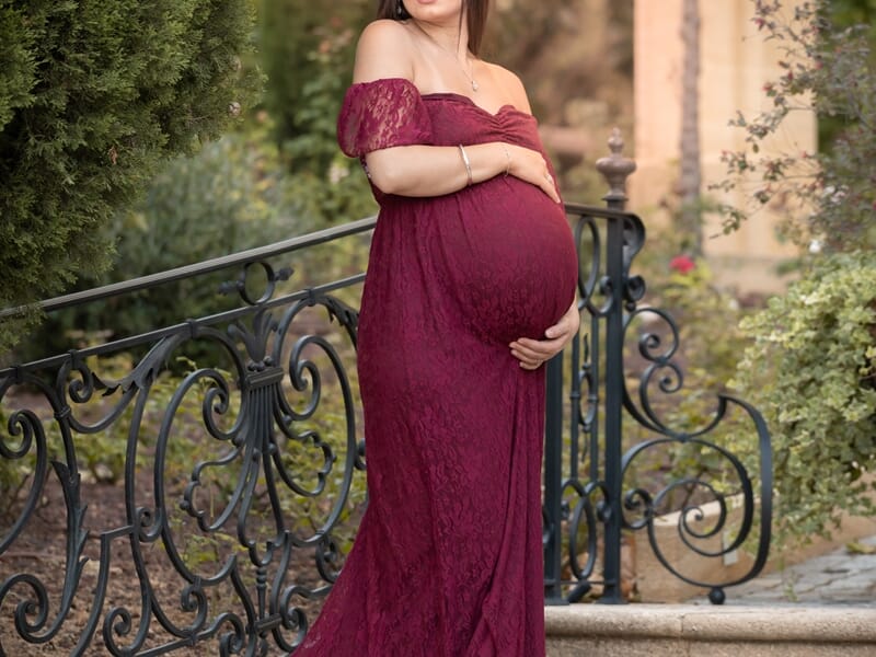 Photo d'une femme enceinte sur un escalier avec une robe bordeau en dentelle et la nature en fond