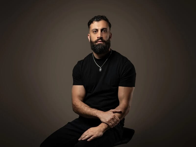 Photo d'un homme barbu avec un t-shirt noir sur fond marron