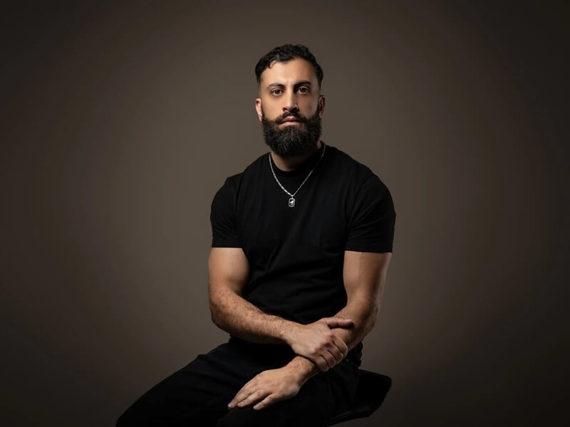 Photo d'un homme barbu avec un t-shirt noir sur fond marron