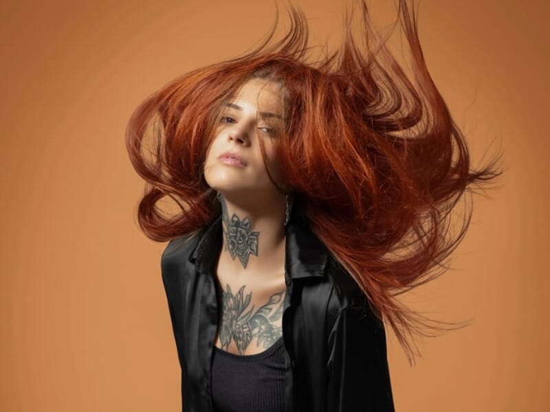 Photo studio d'une femme rousse avec des tatouages sur fond orange et en mouvement
