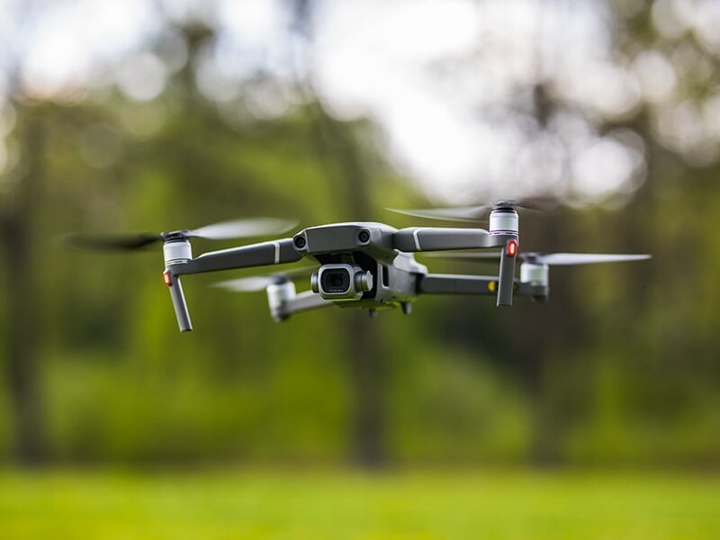 Drone en vol stationnaire en gros plan avec arrière-plan flou d’une forêt.
