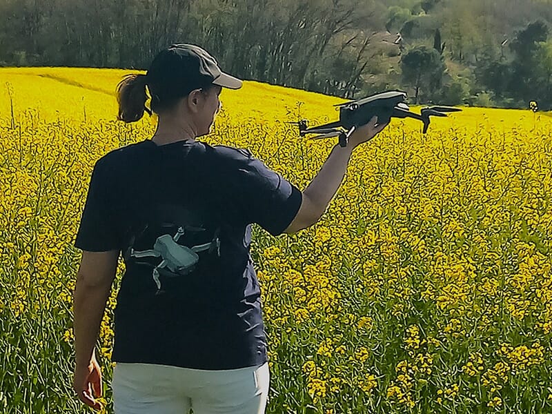 Personne tenant un drone dans un champ de fleurs jaunes, vue de dos avec un t-shirt