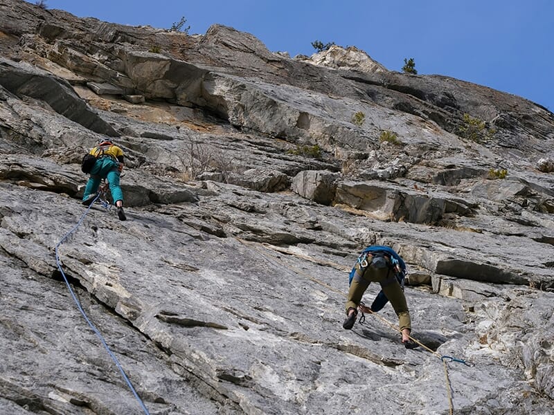 Personnes en escalade sur une grande paroi rocheuse, vue en contre-plongée.