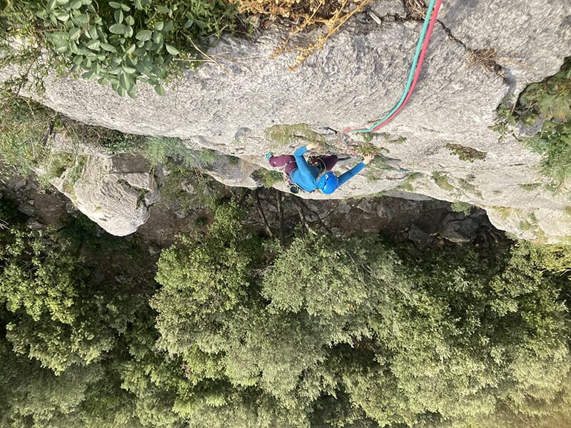 Vue plongeante sur un grimpeur en pleine ascension sur une paroi verticale entourée de végétation.