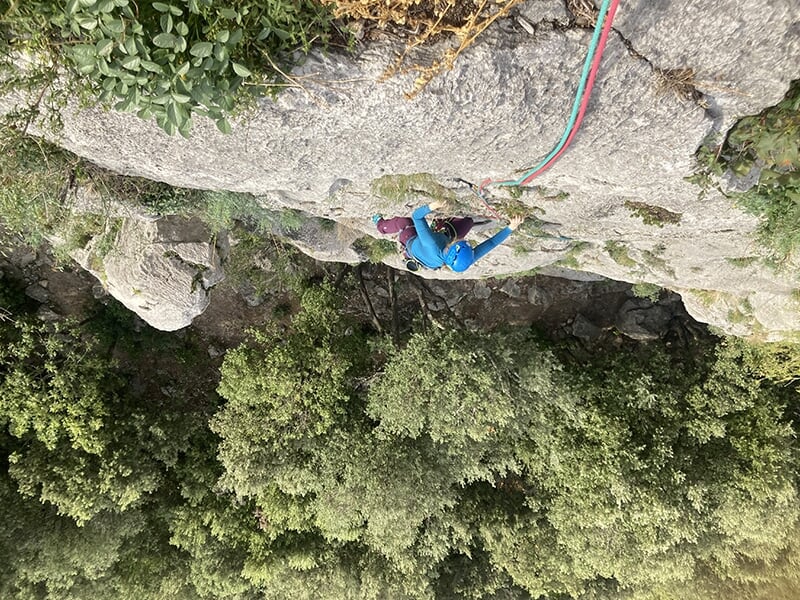 Vue plongeante sur un grimpeur en pleine ascension sur une paroi verticale entourée de végétation.