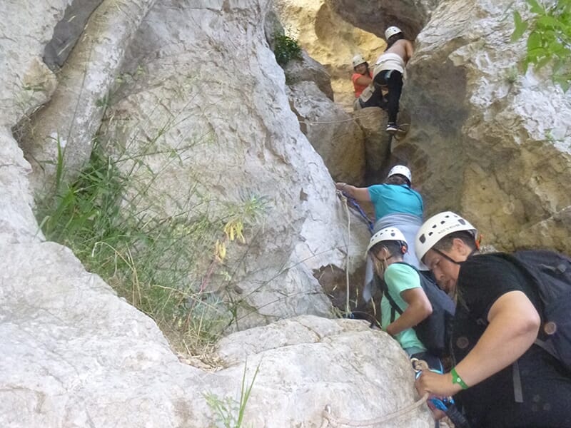 Personnes évoluant sur une paroi rocheuse équipée d’une tyrolienne dans un décor naturel de garrigue.