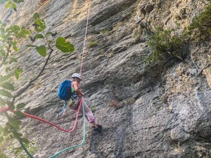 Escalade en falaise d’une grimpeuse en moulinette sur un rocher calcaire, sous un ciel dégagé.