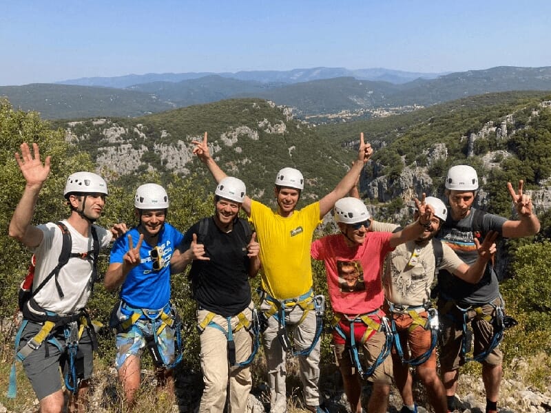 un groupe de personnes équipées pour de l'escalade prennent la pose devant un paysages montagneux