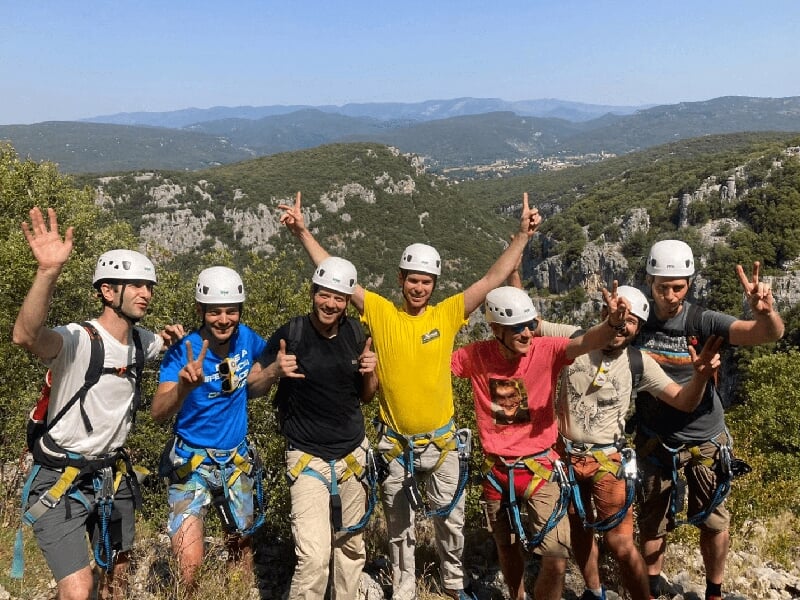un groupe de personnes équipées pour de l'escalade prennent la pose devant un paysages montagneux
