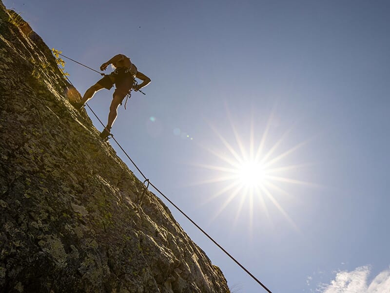Grimpeur en rappel sur une paroi rocheuse, silhouette découpée sous un soleil éclatant.
