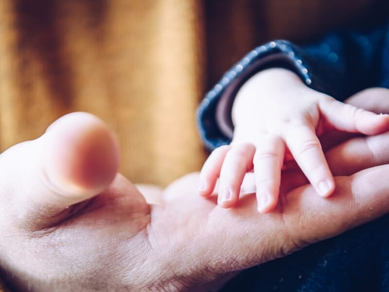 Main d’un bébé posée dans la paume d’un adulte, moment de tendresse capturé en gros plan.