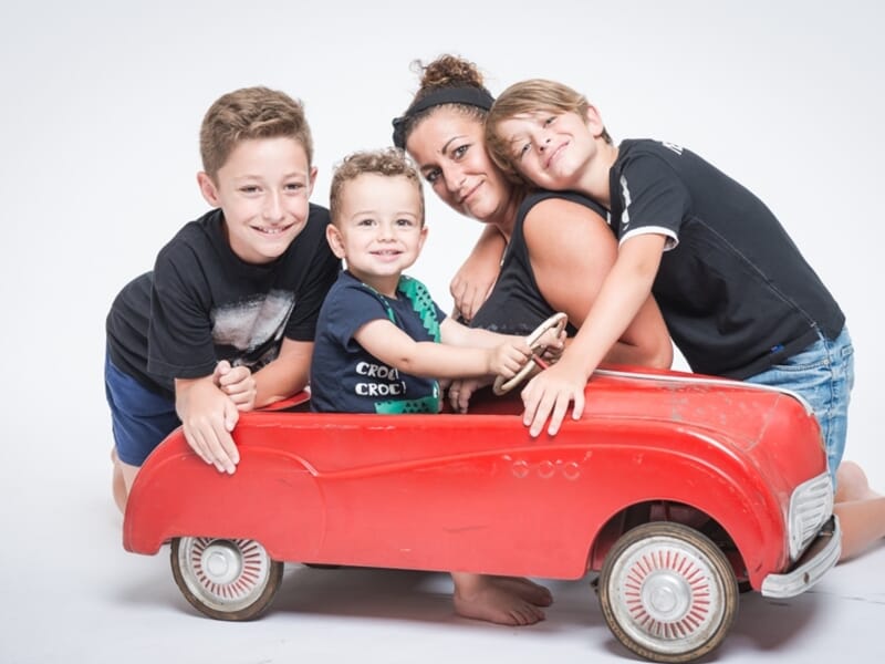 Maman et enfants dans une voiturette rouge, moment complice.