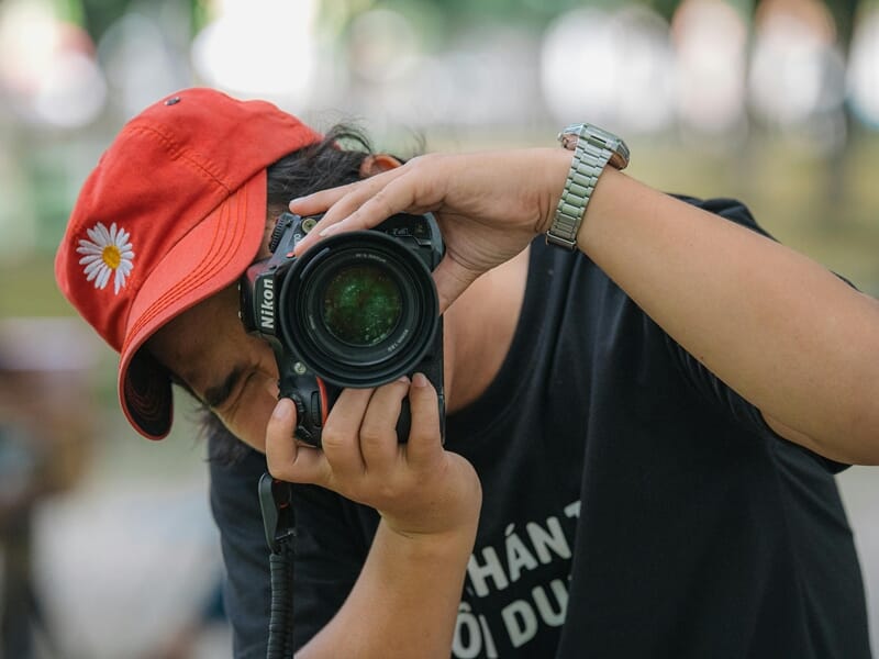 Photographe en casquette rouge ajustant son Nikon, prêt à capturer un instant.