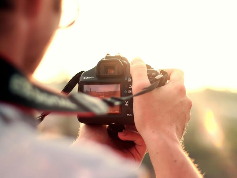 Photographe cadrant une scène avec un appareil Canon au coucher du soleil.