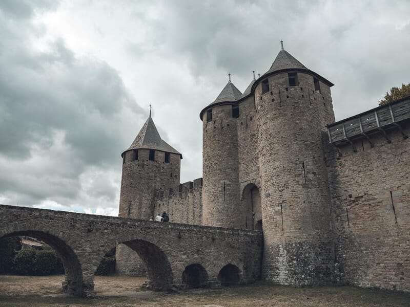 Tour médiévale et pont en pierre de la Cité de Carcassonne sous un ciel nuageux.