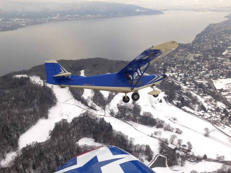 Vue sur un avion ulm en vol au-dessus d'un paysage enneigé, avec en fond un cours d'eau