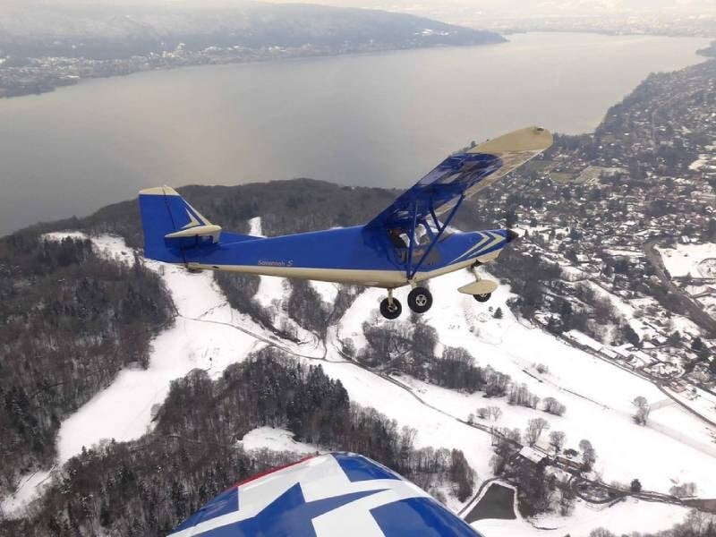 Vue sur un avion ulm en vol au-dessus d'un paysage enneigé, avec en fond un cours d'eau