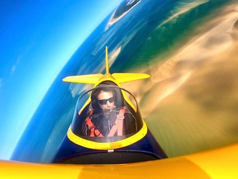 Pilote aux commande d'un avion ULM biplan jaune avec des méandres en fond