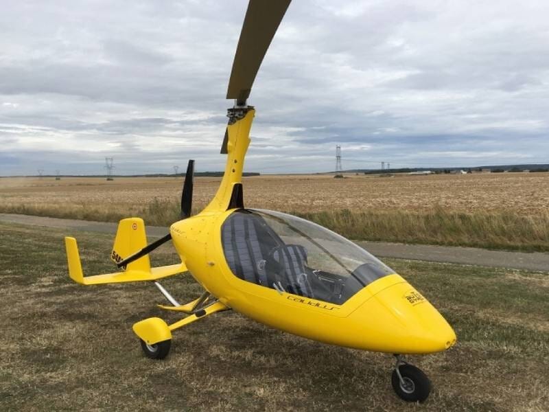 ULM autogire jaune vu de près, posé dans l'herbe à côté d'un champ