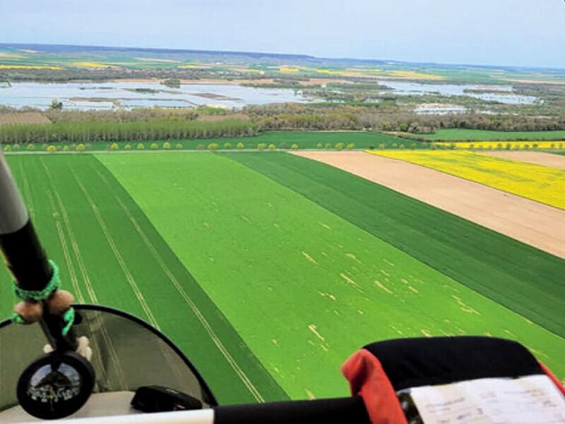 Vue aérienne sur des champs verts et jaunes ainsi qu'un plan d'eau au loin.