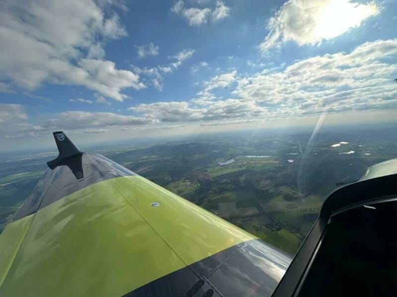Vue sur la campagne environnante, le ciel bleu et les nuages depuis l'aile d'un ULM vert et noir.
