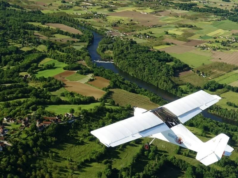 Avion ULM Nynja en vol au-dessus de la campagne verdoyante, sillonnée par un cours d'eau.
