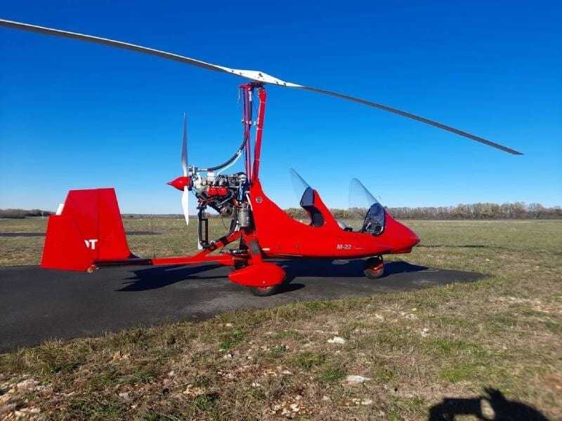 ULM autogire Magni M22 rouge posé sur une piste entourée d'herbe.