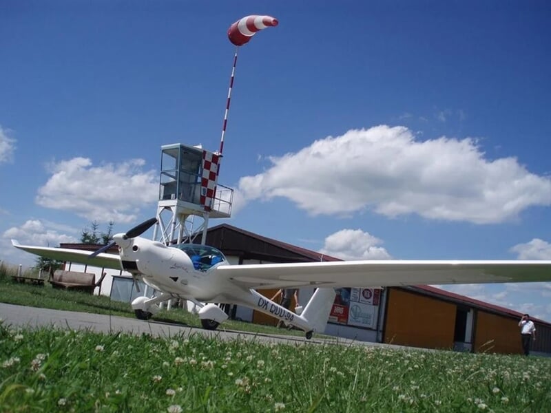Petit avion blanc stationné sur l'herbe près d'un bâtiment avec une tour de contrôle lors d'un vol en avion ULM près de Lyon.