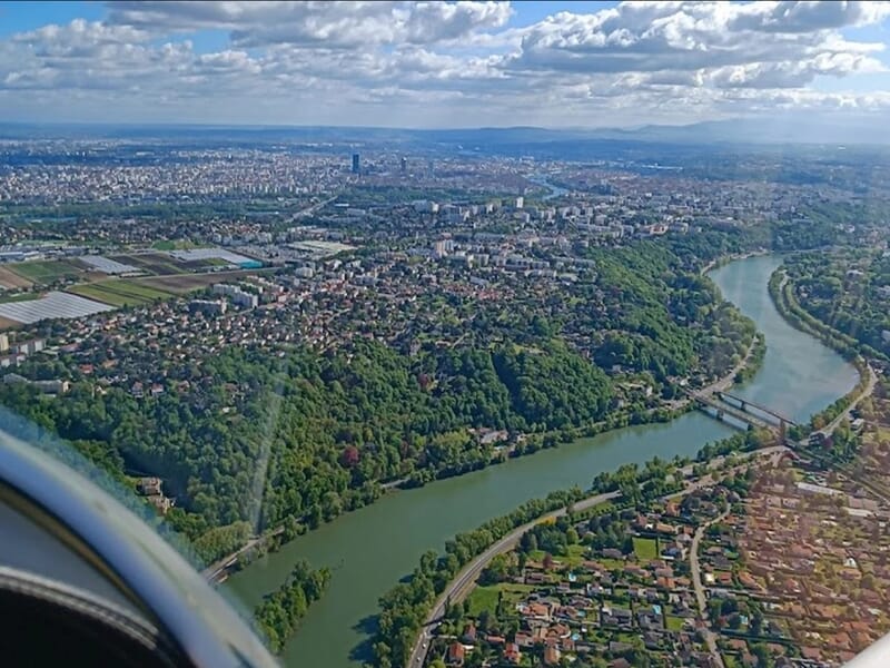 Vue aérienne d'une grande ville avec une rivière sinueuse et des zones vertes lors d'un vol en avion ULM près de Lyon.