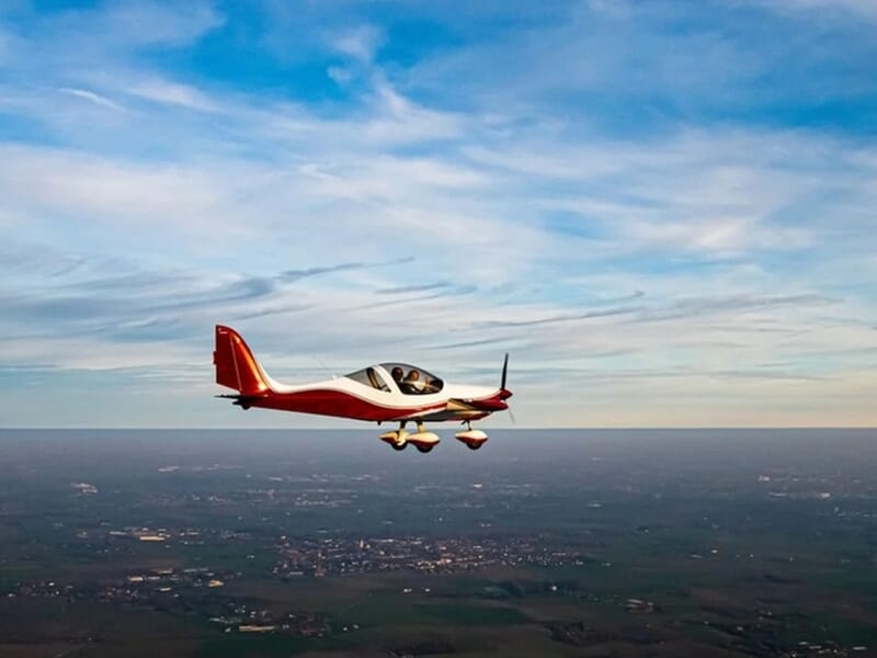 Petit avion rouge et blanc en vol au-dessus d'un paysage rural lors d'un vol en avion ULM à Lens.