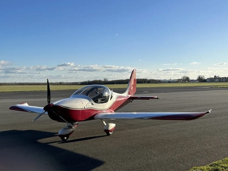 Avion rouge et blanc posé sur une piste d'aéroport avec un ciel bleu lors d'un vol en avion ULM à Lens.