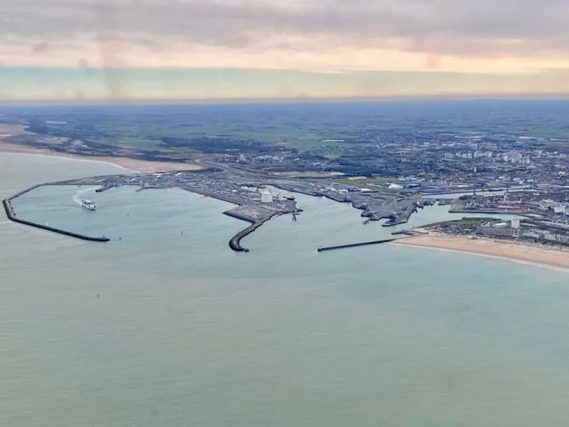 Vue aérienne d'un port avec digues et plage sous un ciel nuageux, lors d'un vol en avion ULM près de Lille.