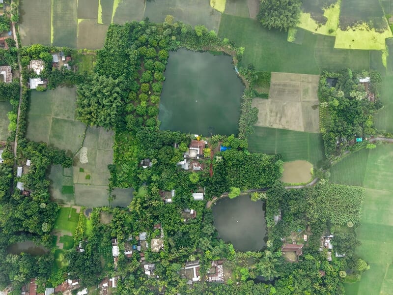 Vue aérienne d'un village entouré de forêts et de plans d'eau, avec des maisons lors d'un vol en ULM près de Briançon.