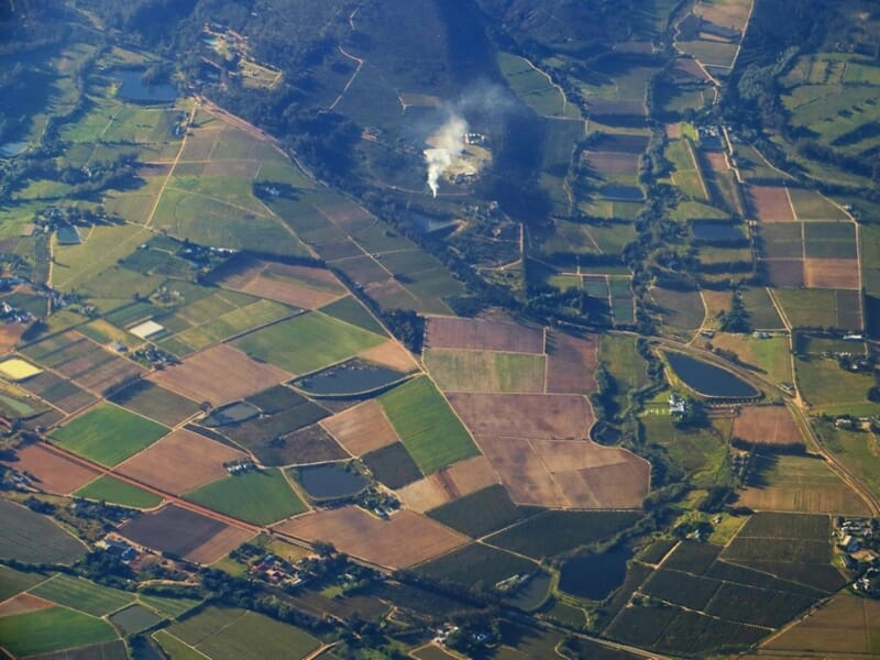 Vue aérienne d'un paysage rural avec champs cultivés et une zone de fumée au centre lors d'un vol en ULM près de Briançon.