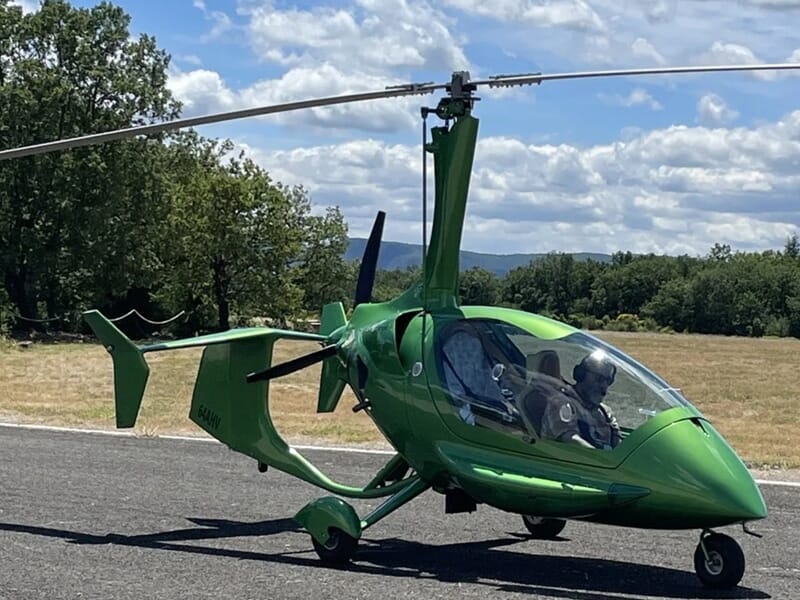 Gyrocoptère vert posé sur une piste avec deux personnes à bord, lors d'un vol en autogire près d'Oloron-Sainte-Marie.