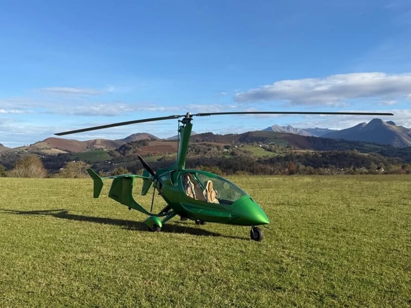 Gyrocoptère vert sur un champ avec montagnes en arrière-plan lors d'un vol en autogire près d'Oloron-Sainte-Marie.