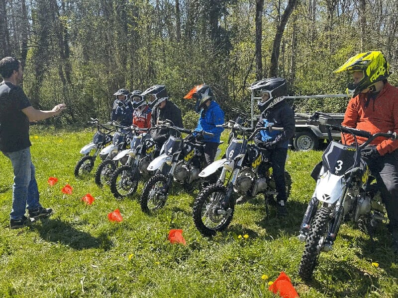 Un groupe de jeunes à moto aligne´ face à un instructeur qui donne des explications, avec des cônes de signalisation au sol.